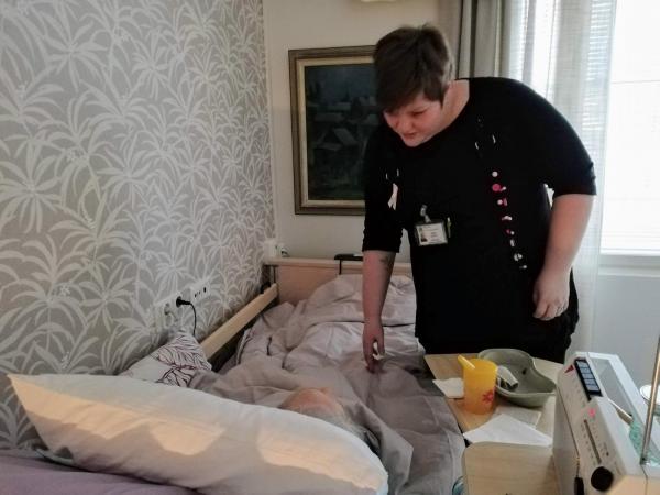 hoitaja auttaa sängyssä makaavaa potilasta